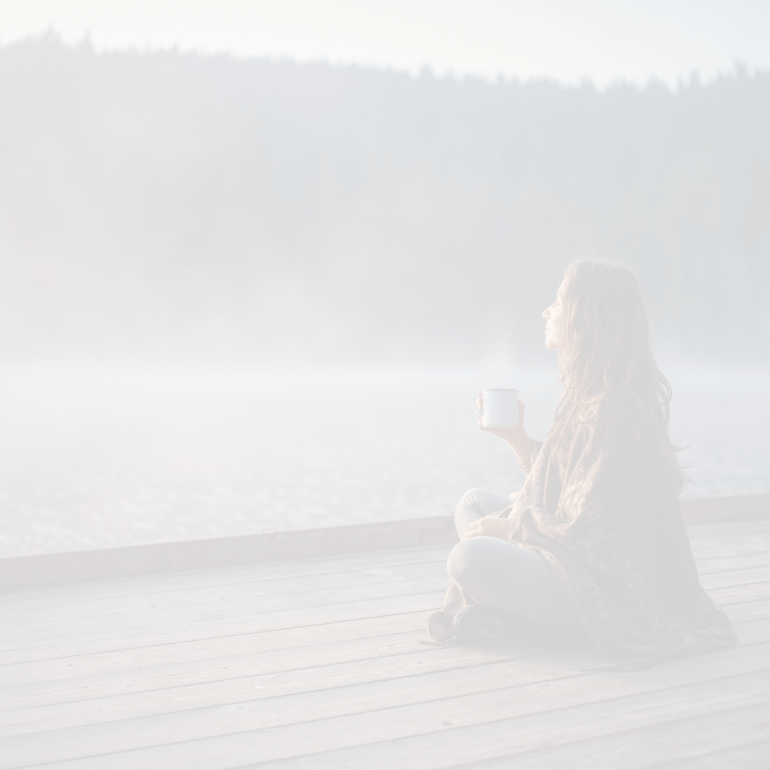 Frau sitzt am See mit einer Tasse in der Hand und blickt in die Ferne als Symbol für Ruhe und Selbstfürsorge