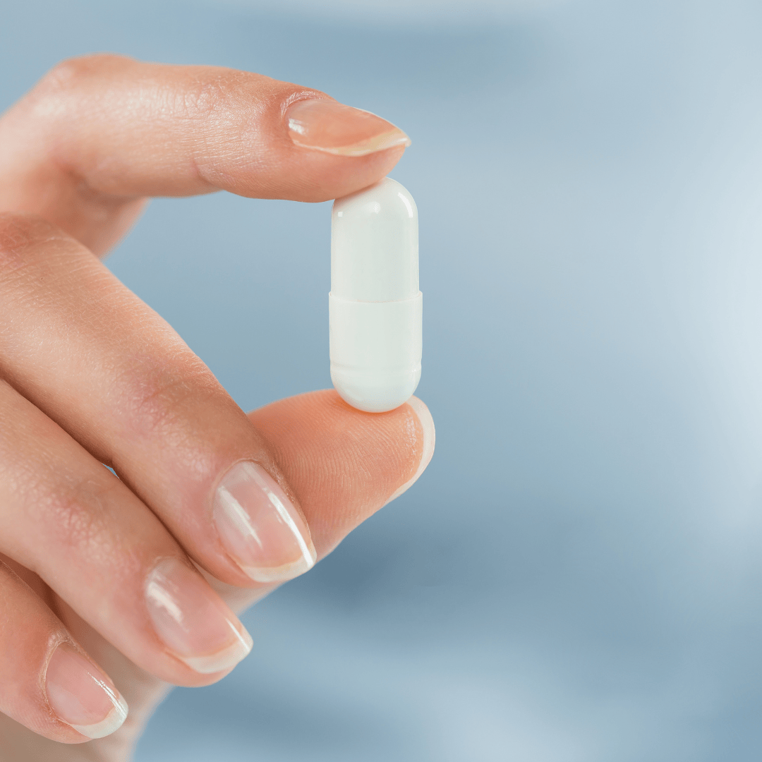 Frau hält eine Magnesium-Kapsel zwischen den Fingern zur täglichen Einnahme